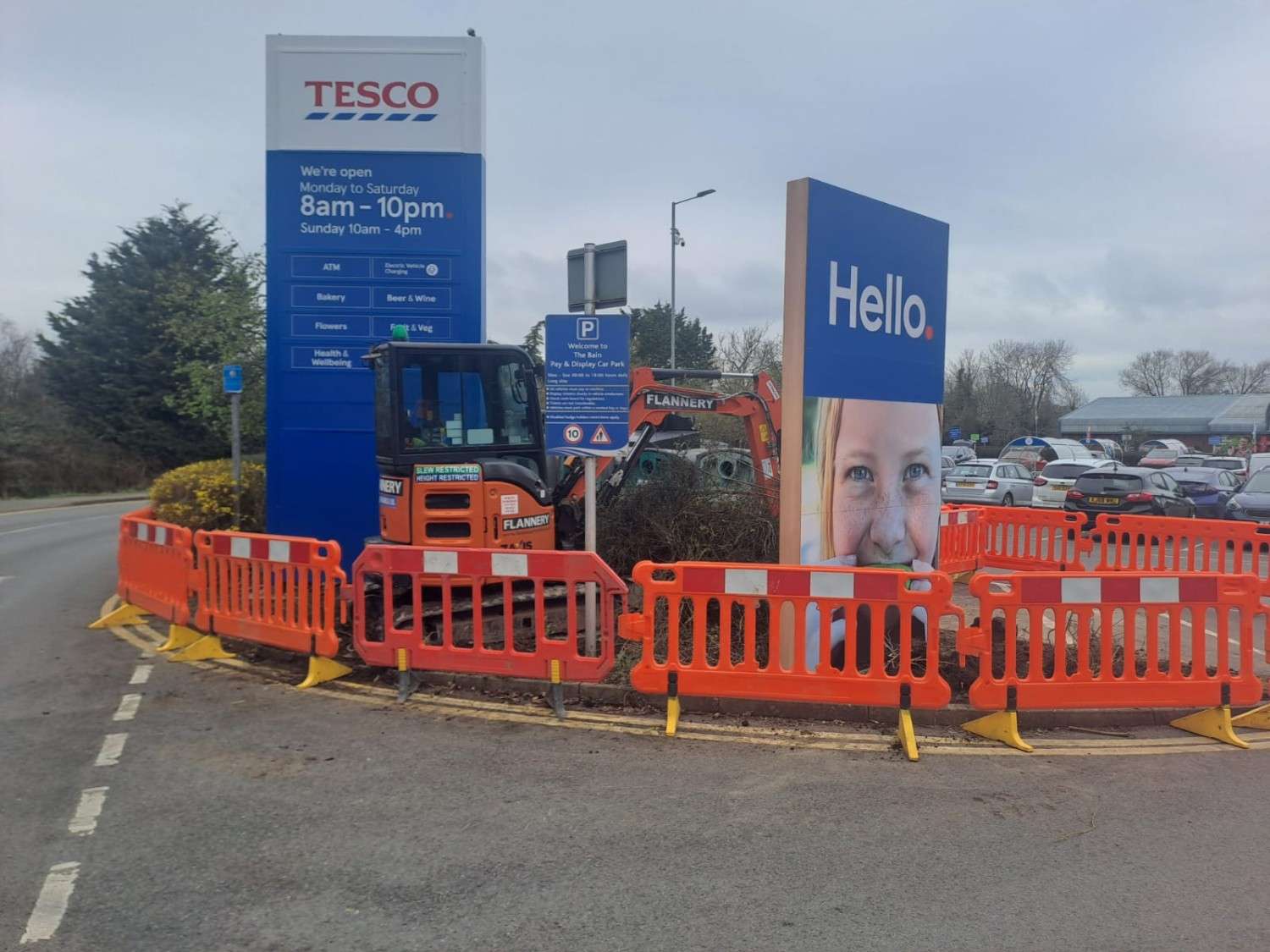 Mini digger working behind traffic barriers in a retail car park