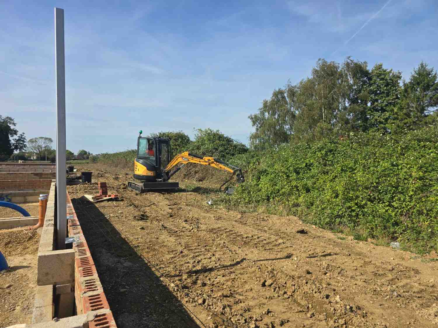 Excavator stripping vegetation along a new boundary wall on a building site
