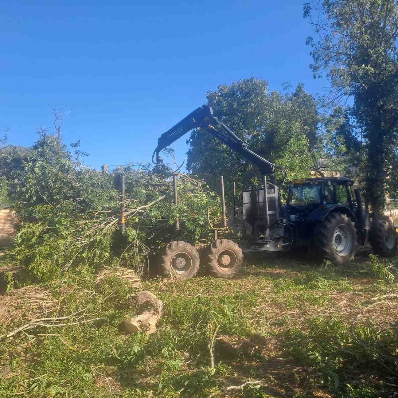 Tractor-mounted timber crane loading brash during land clearance