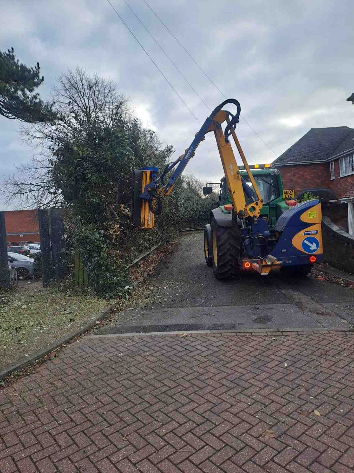 Tractor flail arm trimming an overgrown hedge beside a footpath